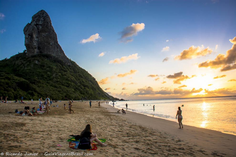 Imagem de varias pessoas nas areias da Praia da Conceição para curtir o por do sol.